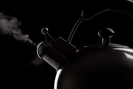 Tea kettle with boiling water over dark background