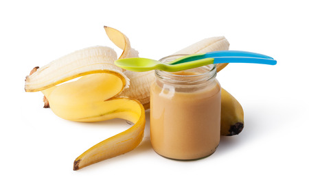 Jar with banana baby food and spoon isolated on whiteの写真素材