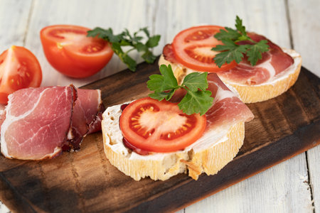 sandwich with prosciutto and tomato on wooden boardの写真素材
