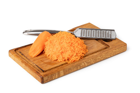 Grated carrots, grater, and a piece of carrot on a wooden cutting board, freshly prepared for cookingの写真素材