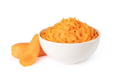 Freshly grated carrots are served in a white bowl next to two pieces of fresh carrotsの写真素材