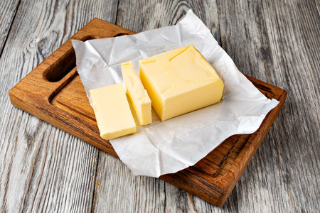 One stick of butter, partially unwrapped from its packaging, sits on a wooden cutting boardの写真素材