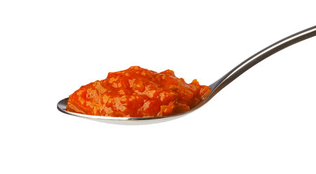 Spoon holding a vibrant red pepper-based vegetable spread on white background