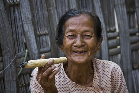Smiling Asiatic woman smoking a cigar  Image taken in a little village near Pagan, in Myanmar  Burma , where a woman does cigars by herself and smoke them proudly in the middle of the street  In these image, she was smiling at me   のeditorial素材