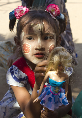Poverty through Childs eye  This images has been taken in a little village in Myanmar  Burma   A girl with the typical Sandal-Saffron cream in face to protect the skin from the sun  She holds a doll, a present from us のeditorial素材