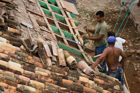 Trinidad, Cuba, August 18, 2012: onstruction workers standing on a roof covering it with wood and tiles tilesのeditorial素材