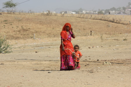 Pushkar, India: A poor Indian Mother orange dressed with her son, standing on the sand in Pushkarのeditorial素材