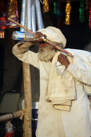 PUSHKAR, INDIA: Indian senior man, white dressed, walking with a cane and a big sack on hos shoulder, at Pushkar Fair in Indiaのeditorial素材