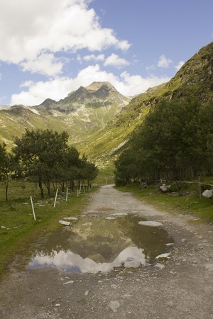 MADESIMO, ITALY - AUG 21 2014: Mountain path in Madesimo valley floor at summer, with mountain reflection in the puddle and and glacier のeditorial素材