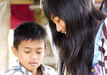 SULAWESI, INDONESIA - JULY 2 2012: Young Indonesian Fruit seller in the South Sulawesi, cleaning fruit, with her brother in the backgroundのeditorial素材
