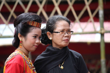 TANA TORAJA, INDONESIA - JULY 3 2012: Two generation of Torajan women,a teenager and a senior, traditionally dressed at a funeral ceremony in Tana Torajaのeditorial素材