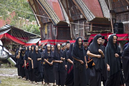 TANA TORAJA, INDONESIA - JULY 3 2012: Women procession at a traditional funeral ceremony, with typical tongkonan house in the backgroundのeditorial素材