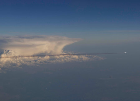 An airplane flying in the sky through the clouds and its contrail. View from another airplane