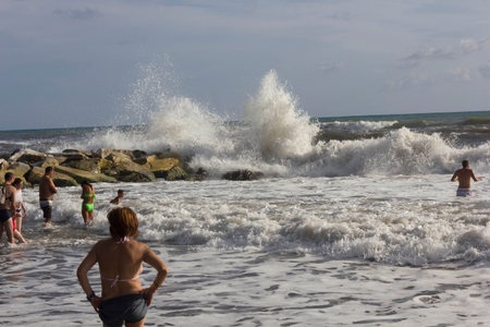 MARINA DI MASSA, ITALY - AUGUST 17 2015: People on the coastlineon a heavy sea day in the summer, with the waves crashing into rocksのeditorial素材