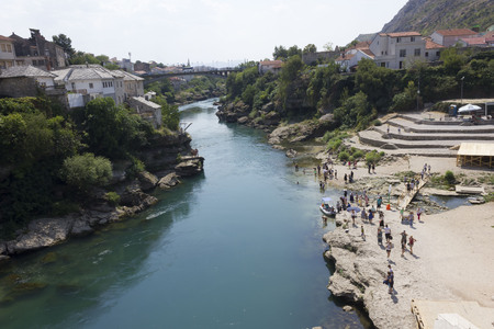 MOSTAR, BOSNIA AND HERZEGOVINA - AUGUST 17 2017: Neretva river in Mostar, with some people along the rocky beachのeditorial素材