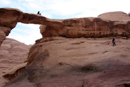 spectacular stone arch and people climbing on it in Wadi Rum desert, Jordanの写真素材