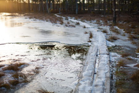 Cold winter sunset background of a bog landscape with a wooden boardwalk heading over a lake covered in iceの写真素材