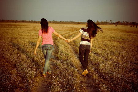woman friend walking hand in hand going in spring fieldの写真素材