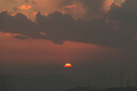 The half of the sunset below clouds with wind-mill generators on mountains in fog faraway.の写真素材