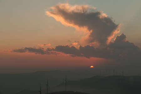 The half of the sunset below clouds with wind-mill generators on mountains in fog.の写真素材