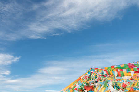 Clear sky with white clouds floating,peacefully.With a tower consist of a lot of colorful prayer flags in the corner as foreground in the morning in Tibet,China.の写真素材