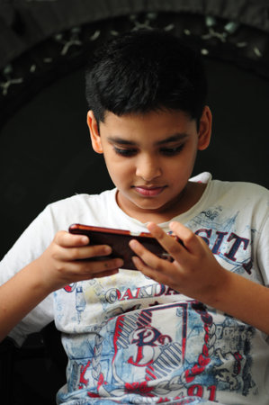 Boy engrossed in playing a game on a mobile phone at home.