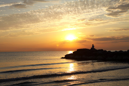 Beautiful sunset at the sea with a lighthouse in the foreground.の写真素材