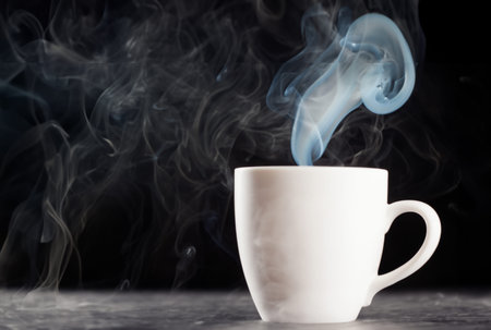 White cup of hot coffee with smoke on black background, close up