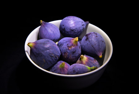 Ripe purple figs in a white bowl on a black backgroundの写真素材
