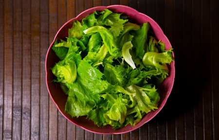 Fresh green lettuce salad in pink bowl on wooden table, top viewの写真素材