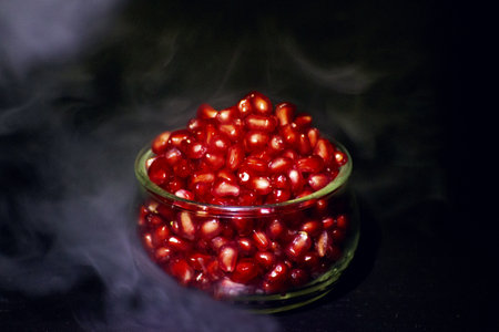 Pomegranate seeds in glass bowl with smoke on black backgroundの写真素材