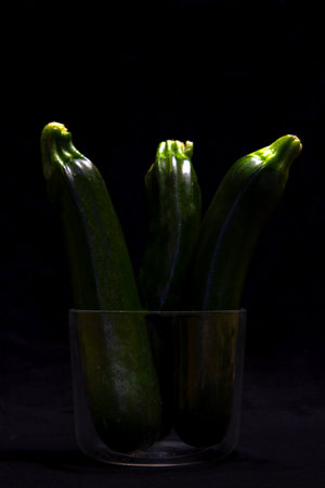 Fresh courgettes in a glass vase on a black backgroundの写真素材