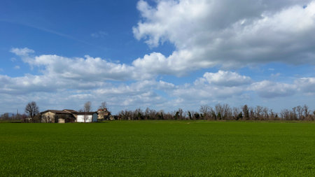 Countryside landscape with a house and a green field under a blue skyの写真素材