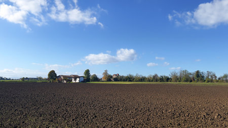 Plowed field with a farmhouse in the background under a blue skyの写真素材
