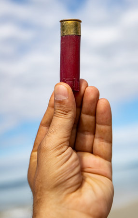 Man's hand holding a red bullet on the background of the sea