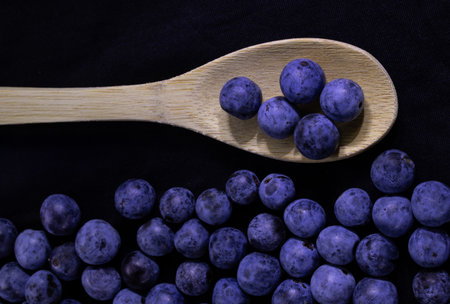 Blueberries on a wooden spoon on a black background. Toned.