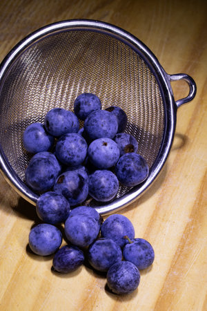 Blue plums in a metal sieve on a wooden table.