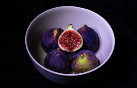 Ripe figs in a bowl on a black background. Selective focus.