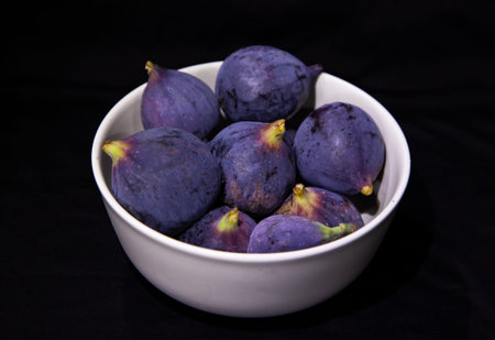 Figs in a white bowl on a black background close-up