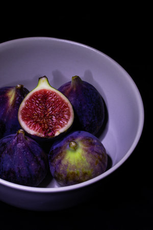Ripe figs in a bowl on a black background. Toned.