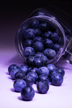 Blue plums spilling out of a glass jar on a purple backgroundの写真素材