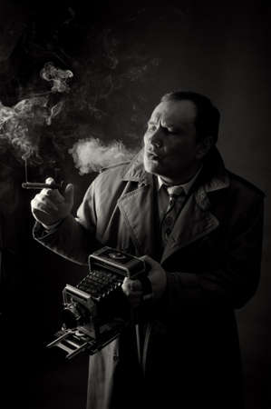 Black and white contrast photo of a retro press photographer with an old camera smoking a sigar の写真素材