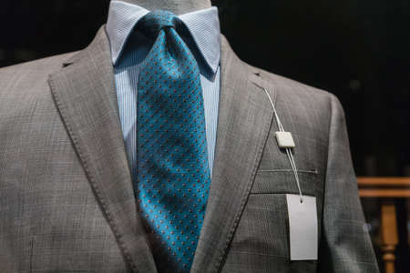 Close-up of a light gray checkered jacket with striped blue shirt, teal tie and a blank white tag on the left lapel の写真素材