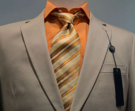 Close-up of a beige jacket with orange shirt, striped tie and a blank black tag on the left lapel の写真素材