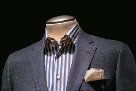 Close-up of a gray checkered jacket with blue   yellow striped shirt and cream handkerchief on black...