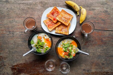 Congee with minced pork and slices of bread and delicious strawberry jam is a favorite breakfast for Thai people. on wood table texture. Top viewの写真素材