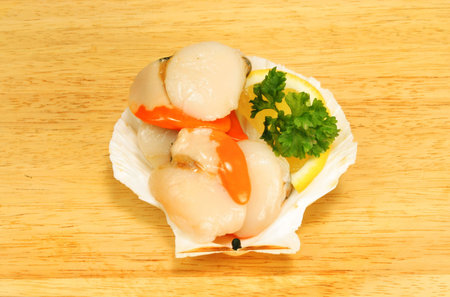 Raw scallops with garnish in a shell on a wooden board