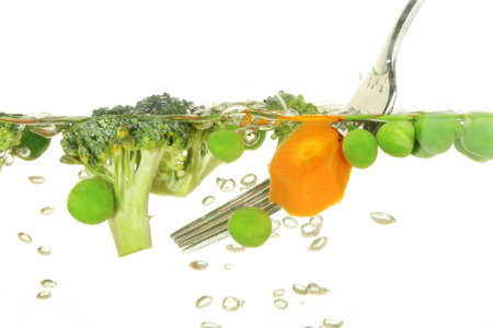 vegetables, carrots, peas and brocolli cooking in boiling water stirred with a fork