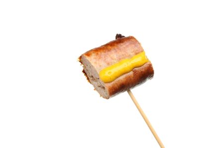 Piece of sausage with mustard on a cocktail stick isolated against whiteの写真素材