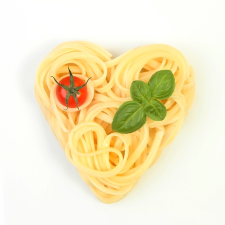 Healthy food, spaghetti in a heart shape with tomato and basil on a white backgroundの写真素材